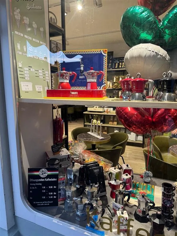 Schaufenster vom Kaffeeladen e Gelateria mit Espressokannen, Ballons in Italienfarben und Öffnungszeiten-Aushang