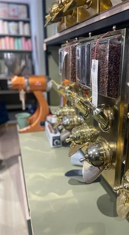 Kaffeebohnen in Glasbehältern mit Messingfassungen über der Theke, dahinter eine große Mühle
