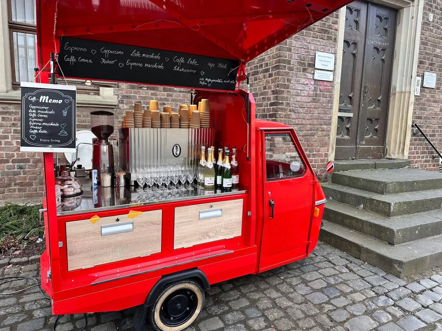 Rote Piaggio Ape als mobile Espressobar mit Getränketafel, Gläsern und Bechern vor dem historischen Rathaus Lechenich