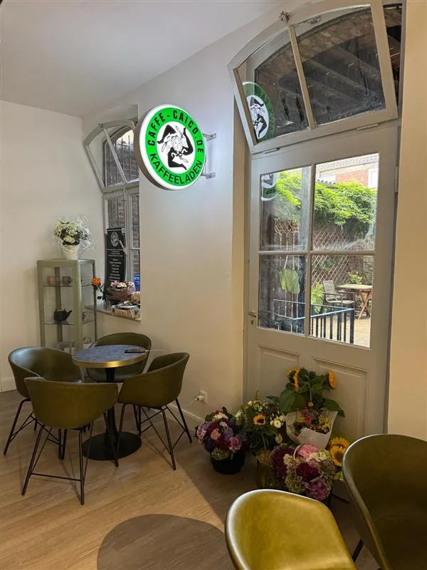 Sitzbereich im Caffe-Caico mit olivgrünen Sesseln, rundem Tisch und leuchtendem Wandlogo