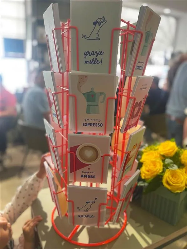 Drehständer mit Grußkarten zu Kaffee und Italien neben einem Strauß gelber Rosen